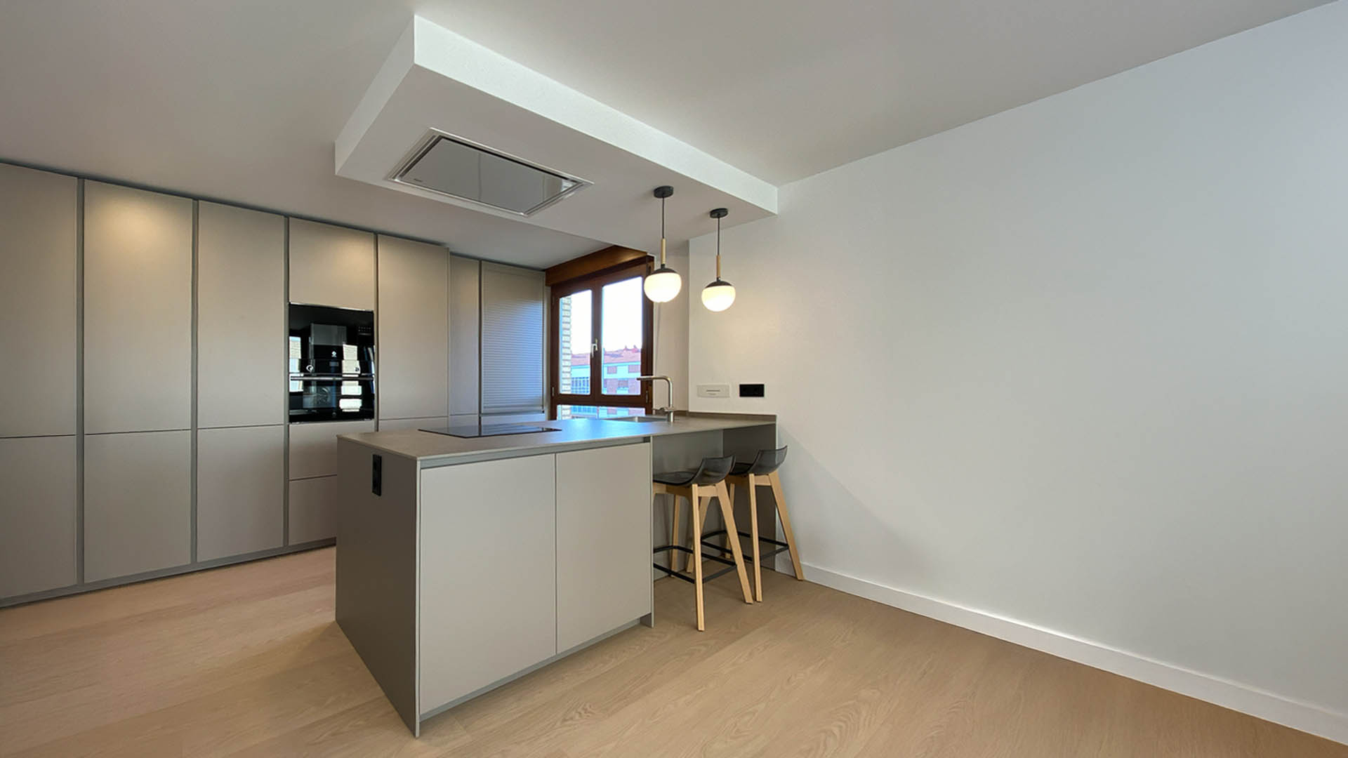 Vista completa de cocina abierta con mobiliario sin tiradores sistema gola, encimera pétrea y suelo de madera natural