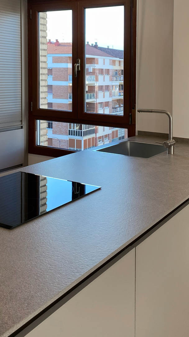 Barra con taburetes en cara posterior de península, configurando zona social integrada en cocina abierta