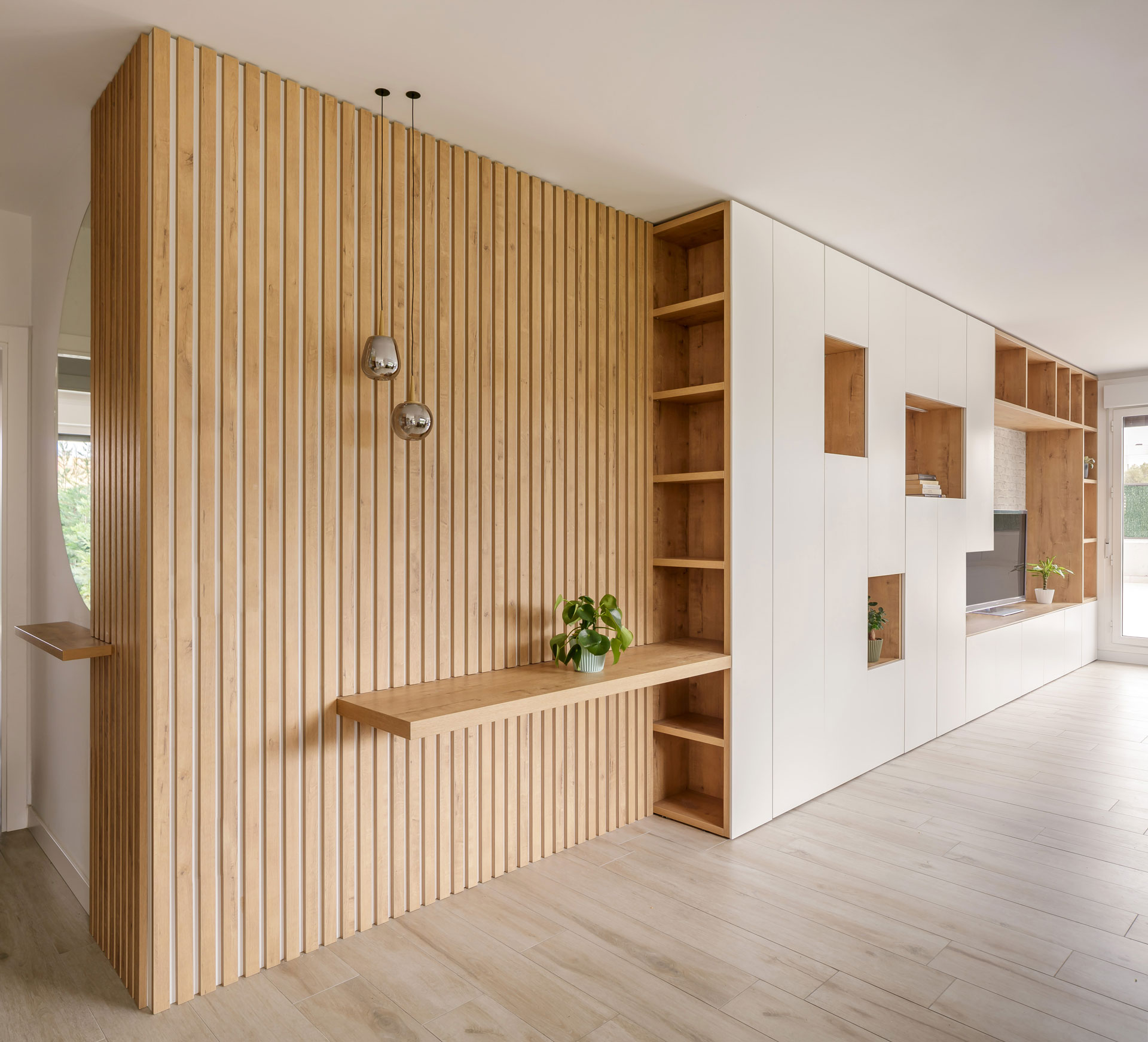 Vista completa de mobiliario continuo desde zona de entrada hasta salón con acabados en tonos claros y madera natural