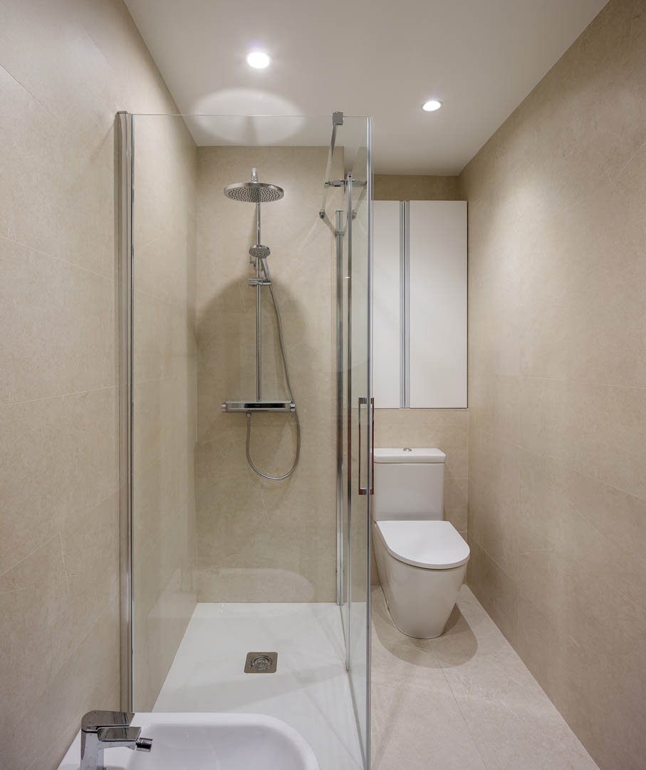 Vista completa de baño principal con bañera exenta, mueble suspendido blanco de doble lavabo, continuidad visual con dormitorio y diseño integrado en vivienda Vitoria