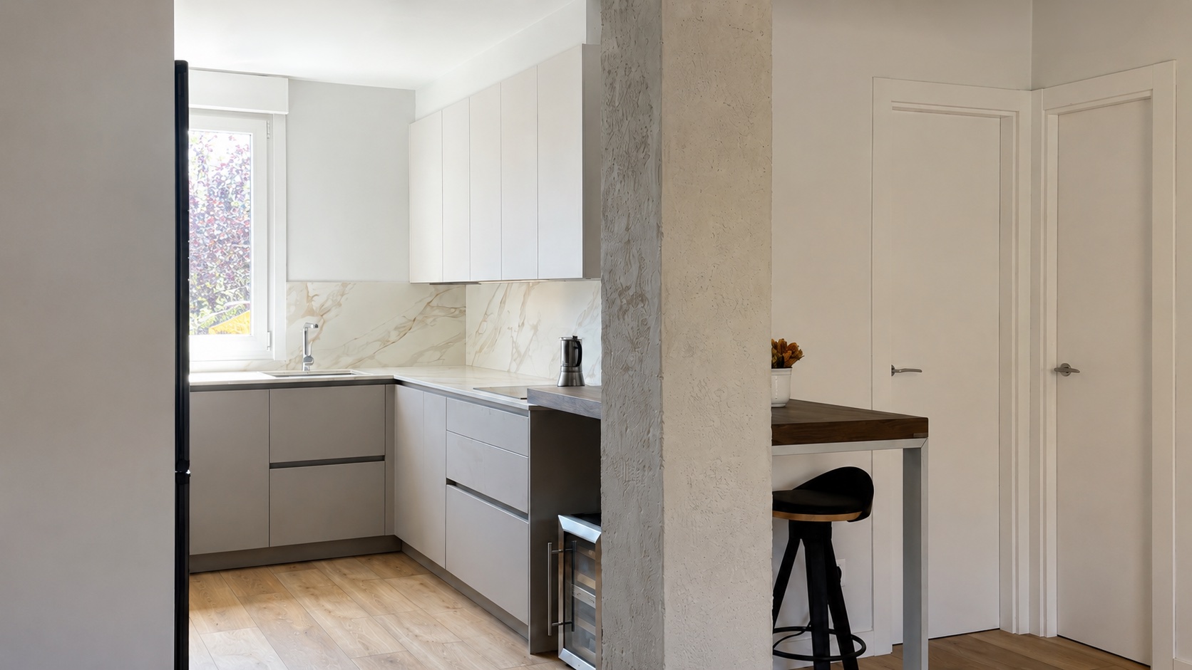 Cocina abierta al salón en la reforma integral OLLER 09 con pilar de hormigón visto, barra de madera con taburete y carpintería lacada en blanco